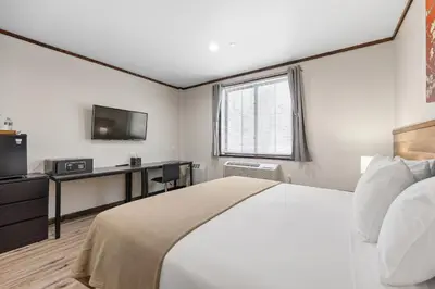 a bedroom with a bed and a desk and a television at Highbridge Hotel in Bronx