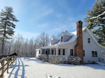 a white house with a brick chimney in the snow at The Suite at Liberty Woods in Belchertown