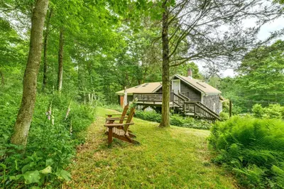 a cabin in the woods with a bench in the grass at Cozy Catskills Vacation Rental with Deck! in Fleischmanns