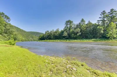 a river next to a grassy field with trees at Pet-Friendly Hancock Home on the Delaware River! in Starlight