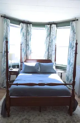 a bedroom with a bed with blue curtains and windows at Charming Victorian Home In Historic District in Newburgh